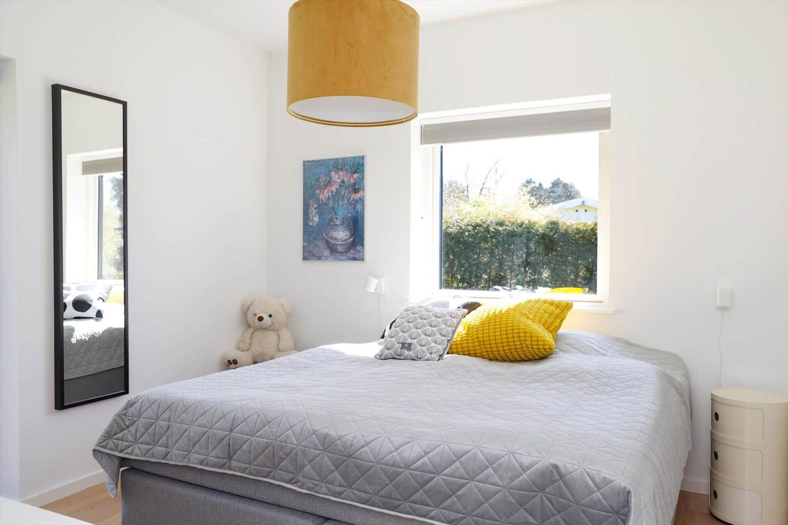 Bedroom with bed, window, mirror, and stuffed bear.