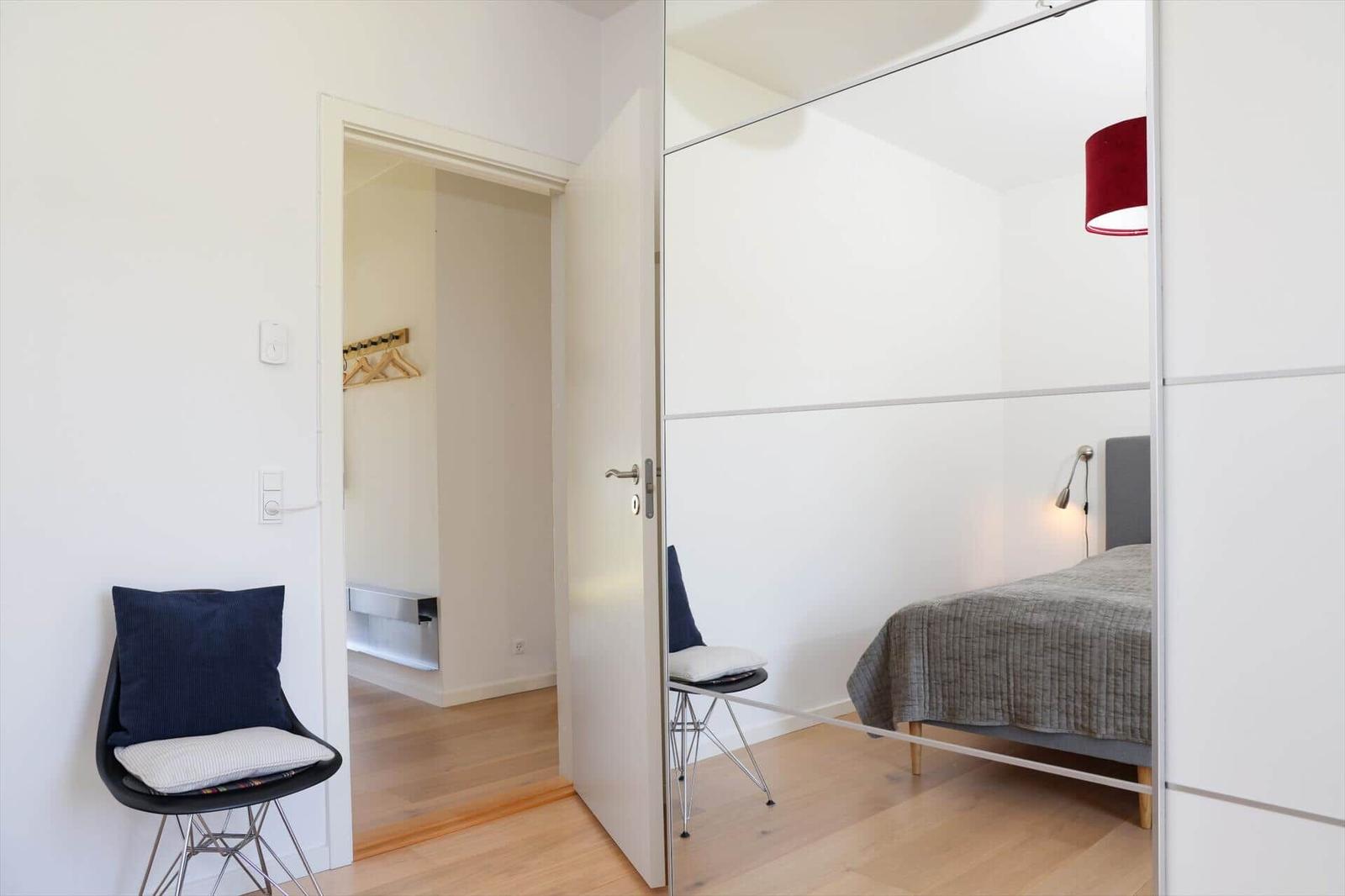 Bedroom with mirrored closet, bed, and chair. Closet with hooks in the background.