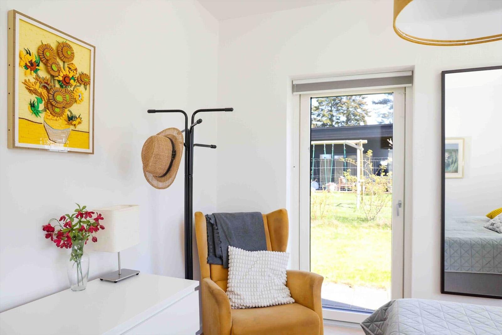A room with a yellow chair, wall art, and view of the garden.