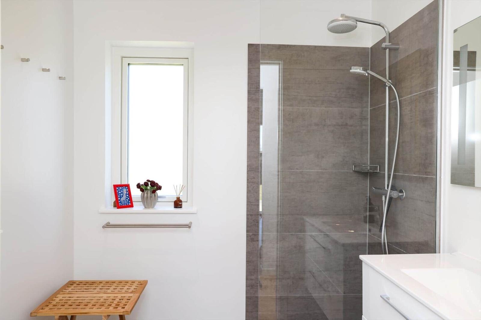 Bathroom with shower, window, and sink. Wooden stool and decor on windowsill.