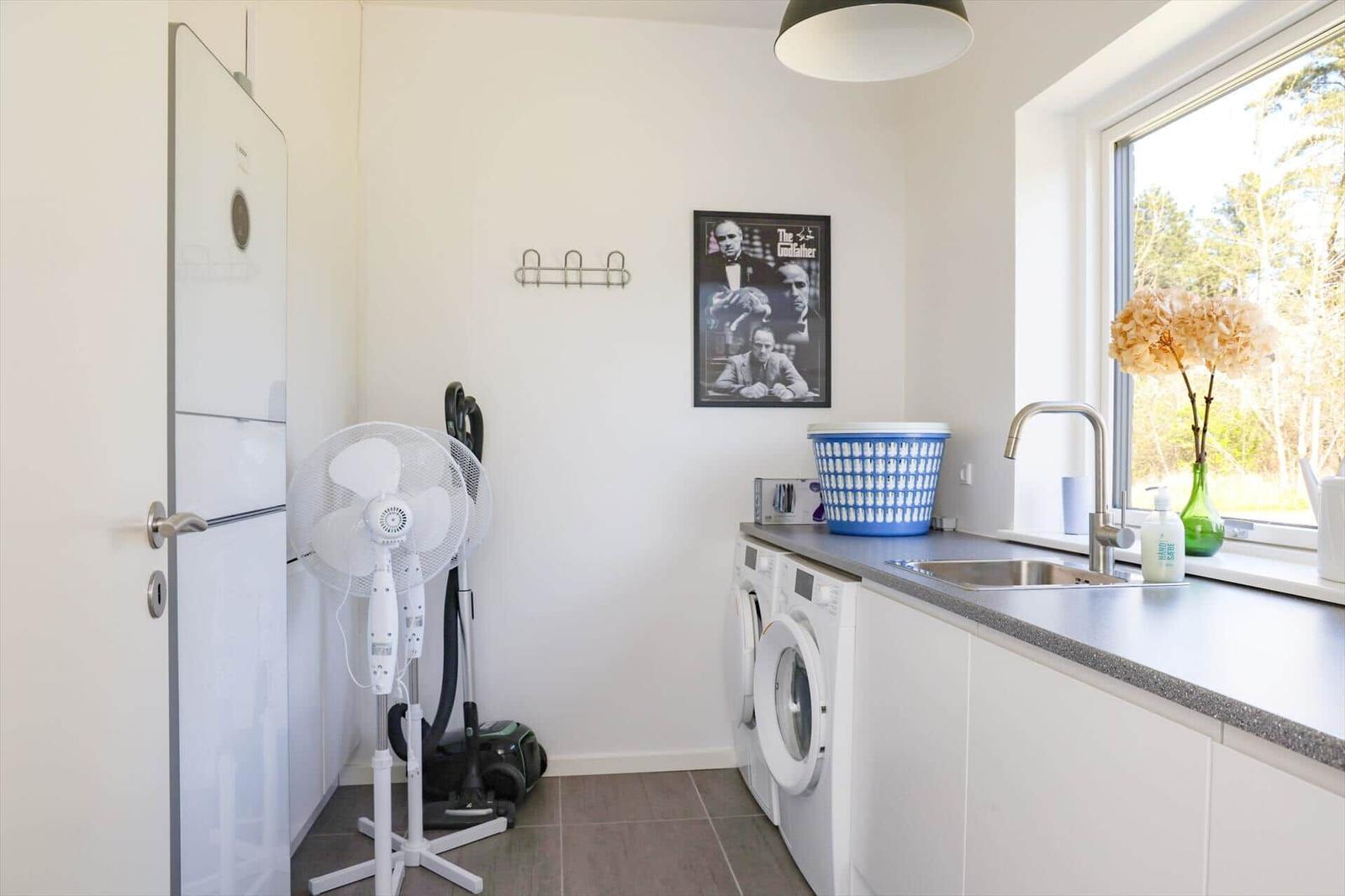 Room with washing machine, sink, and window with view of forest.