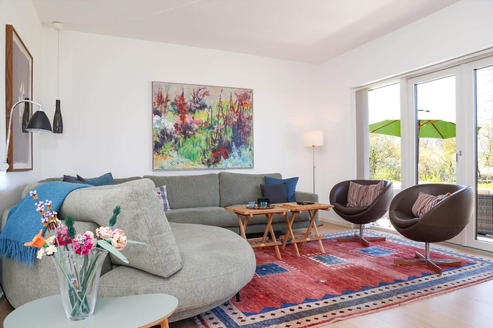 Living room with sofa, two chairs, rug, and wall art. Entrance to terrace with umbrella.