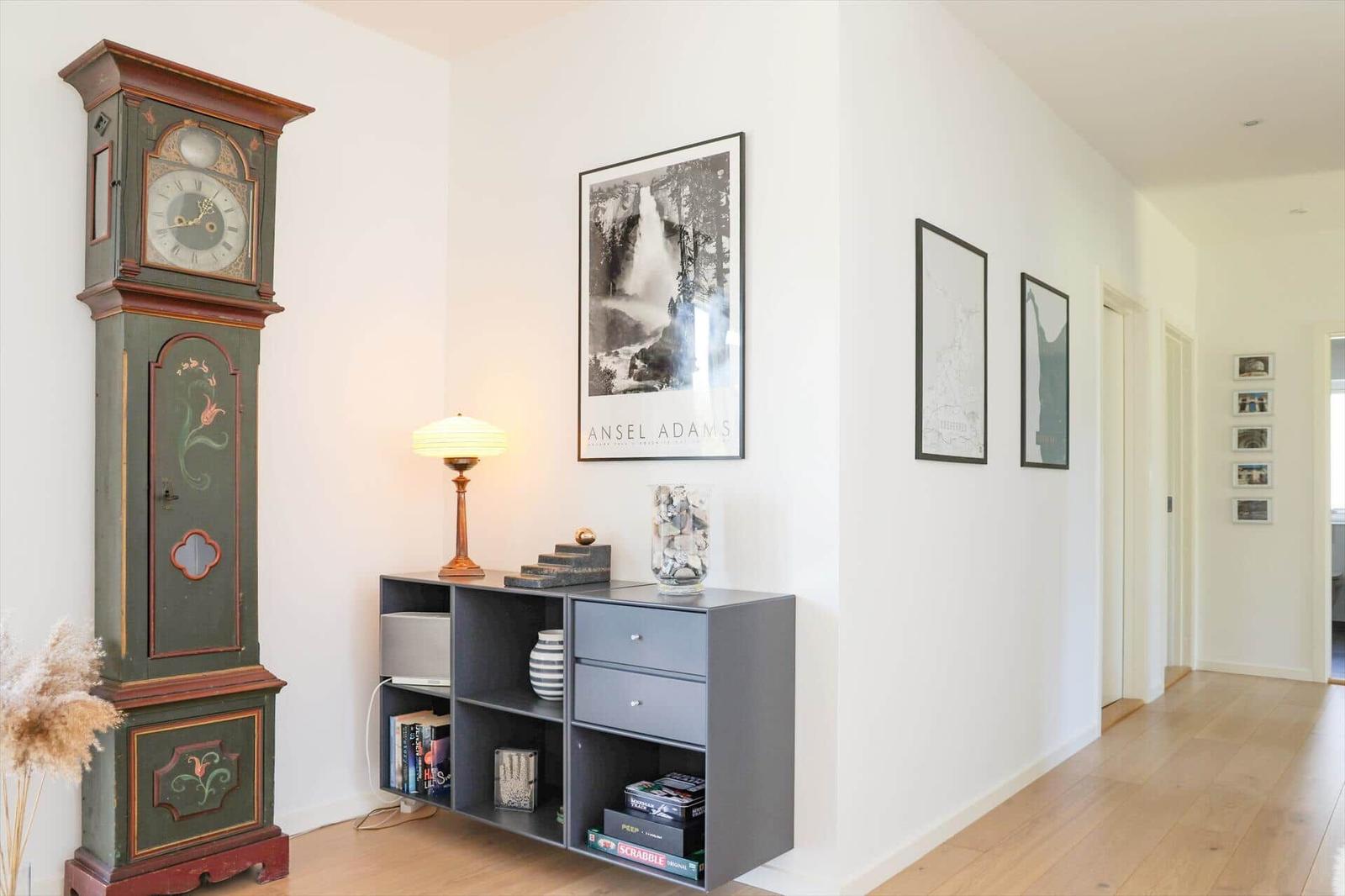 Hallway with antique grandfather clock, framed photos, and gray sideboard with books and games.