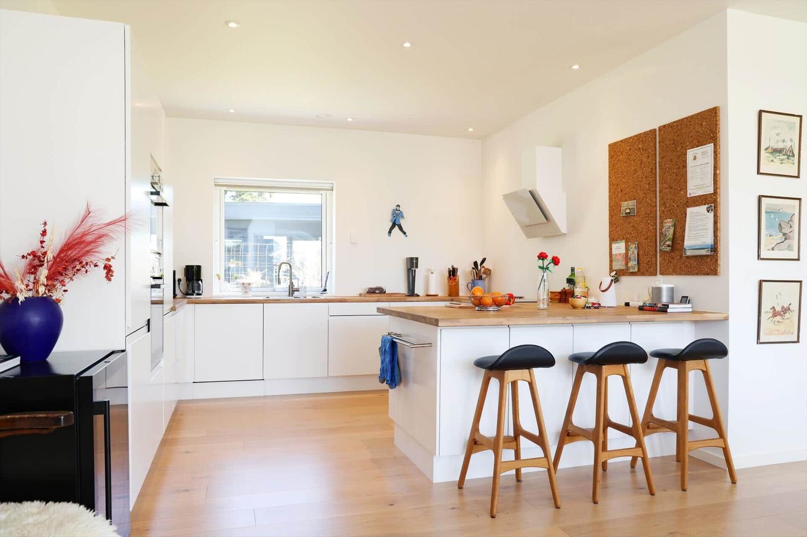 Kitchen with wooden surfaces, white cabinets, and bar stools. A corkboard hangs on the wall.