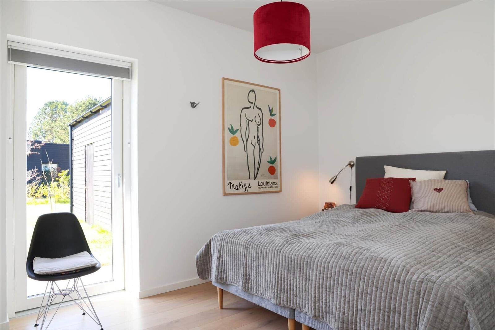 Bedroom with bed, red pendant lamp, and artwork on wall. Door leads outside.