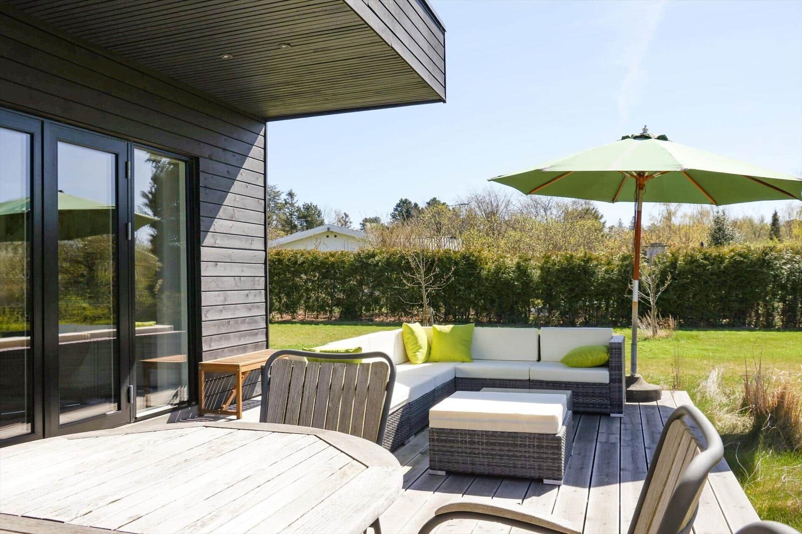 Terrace with seating, umbrella, and table. View of green lawn and hedge.