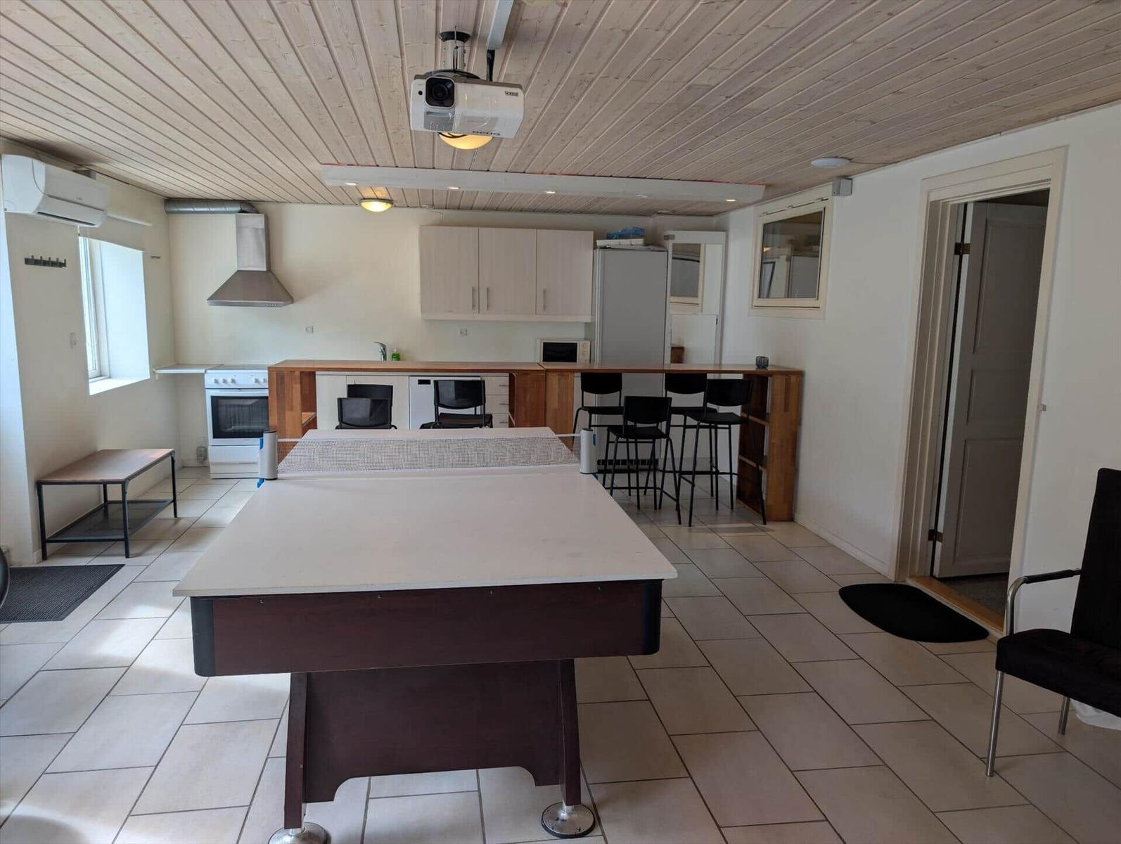 Room with ping pong table, kitchen, and bar stools.