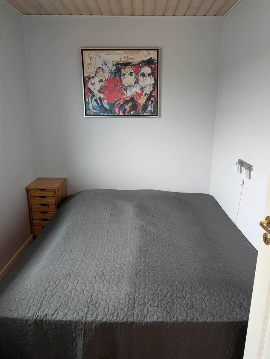 A bedroom with a bed, a wooden dresser, and a picture on the wall.