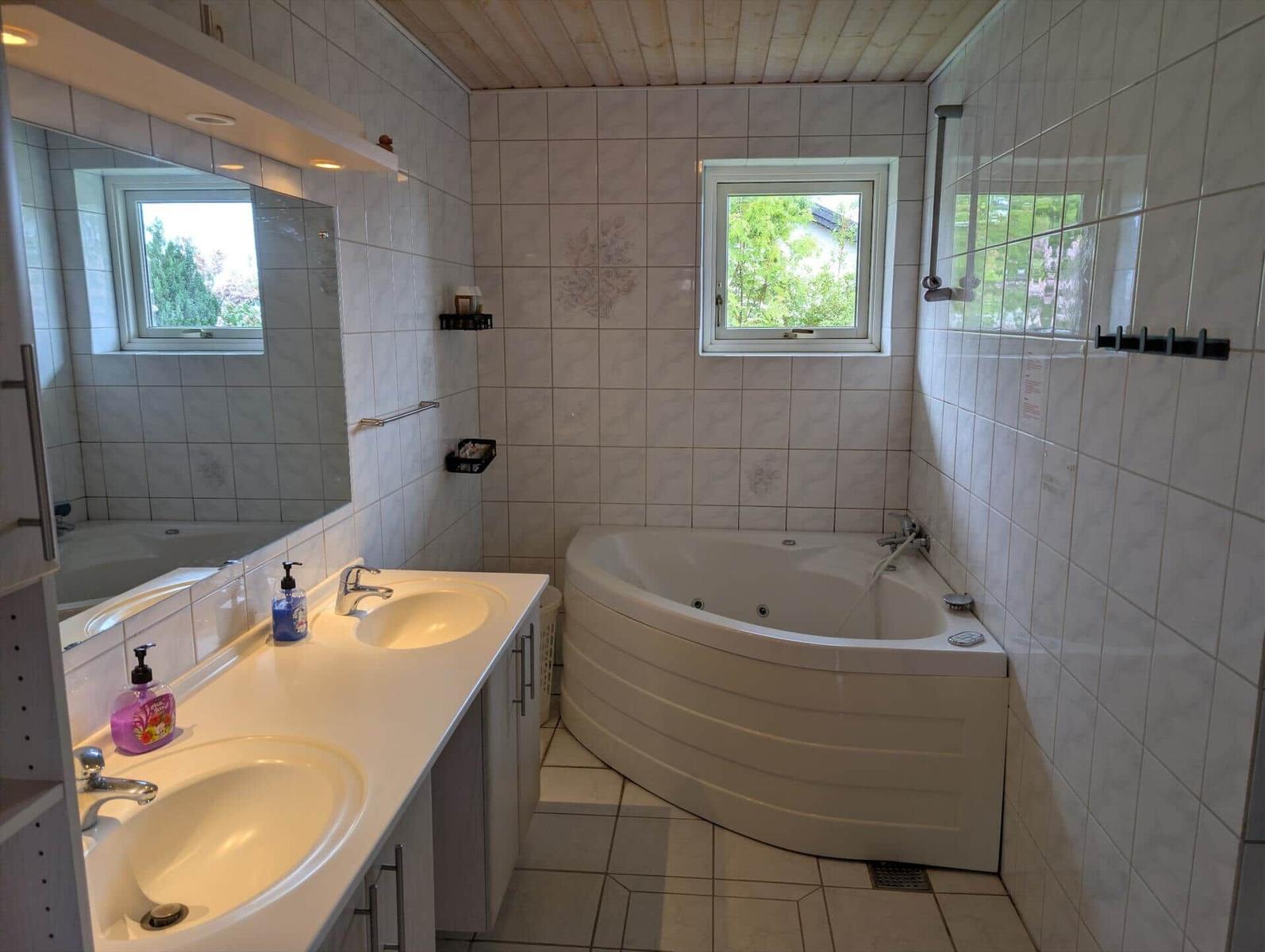 Bathroom with double sink and whirlpool bath. Window with view of greenery.