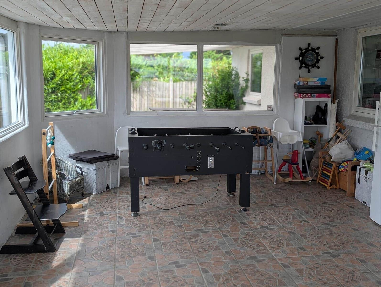 Room with foosball table, childrens toys, and windows to the outside.