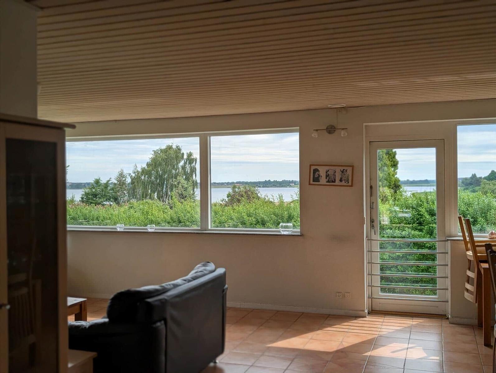 Living area with water and green view, black sofa, terrace door and windows.