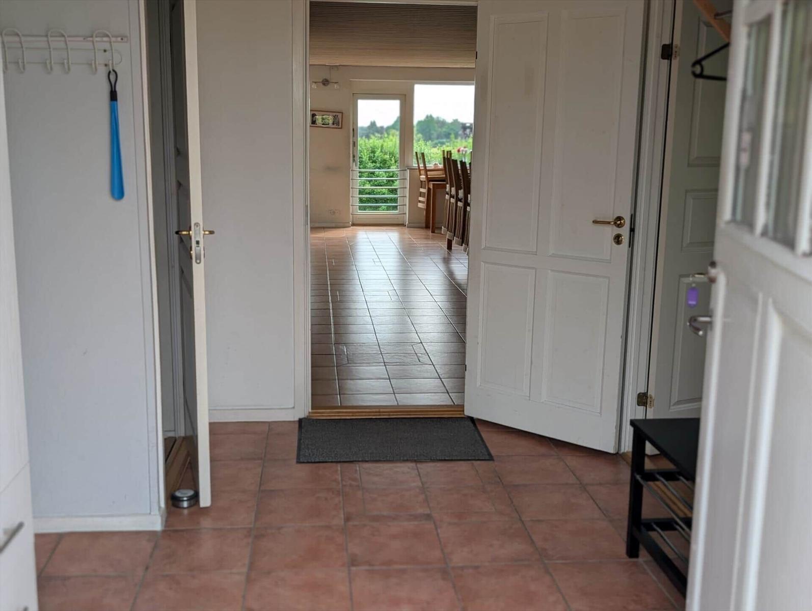 Entrance area with door and tiled floor. Corridor leads to living area with table and chairs.
