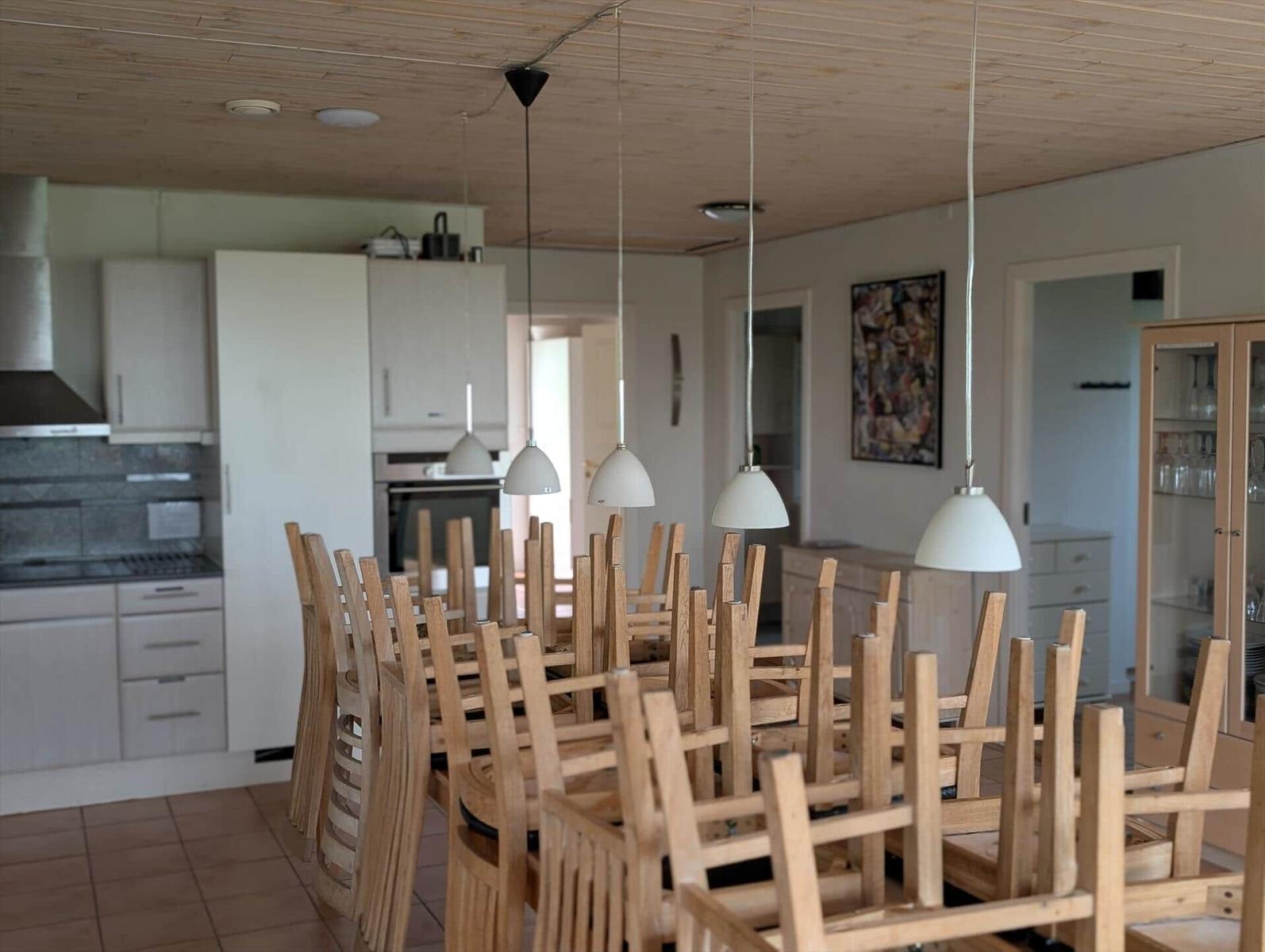Large dining area with wooden chairs and pendant lights. Kitchen in the background.