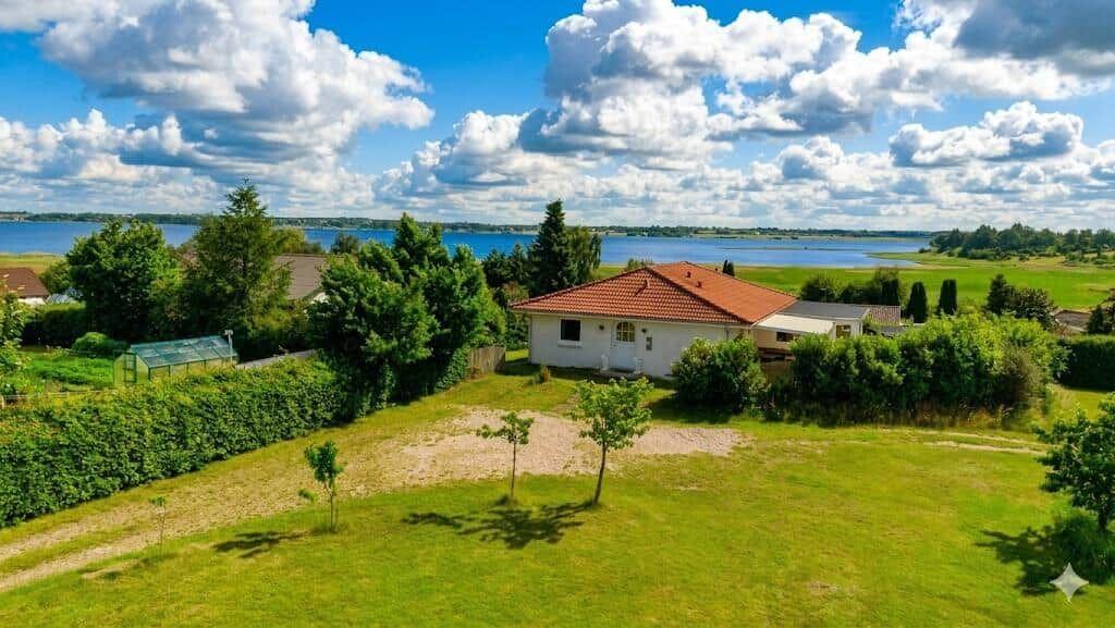 House with red roof, surrounded by lawn and overlooking water.