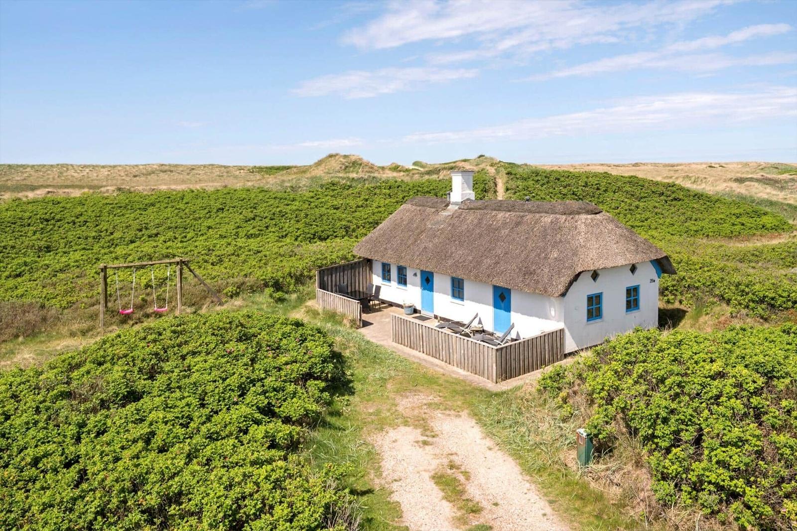 Wohnhaus mit Strohdach und blauen Fenstern in grüner Landschaft