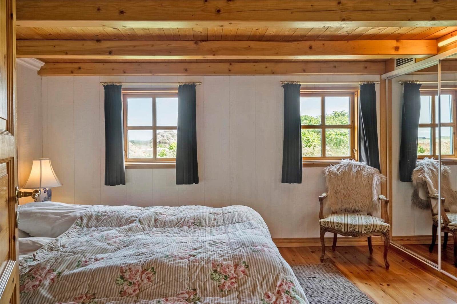 Schlafzimmer mit Bett, Stuhl und Fenstern mit Blick auf die Landschaft.