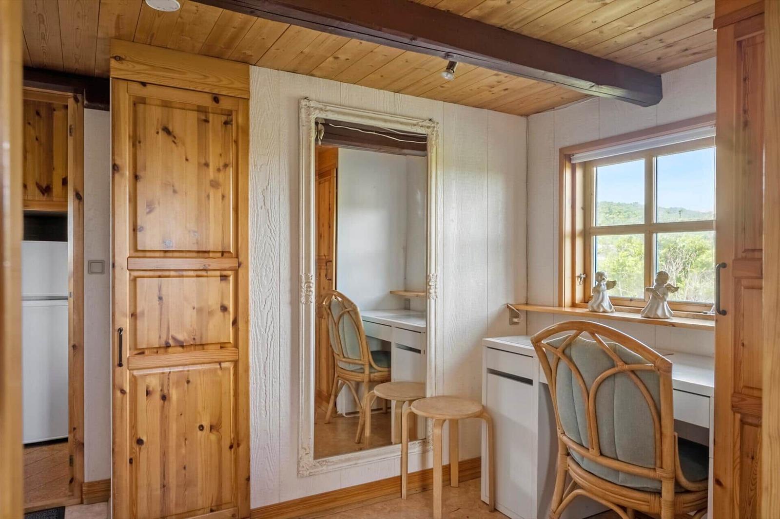 Ein Raum mit Holzwand, Spiegel, Schreibtisch und Stuhl. Fenster mit Blick auf Landschaft.