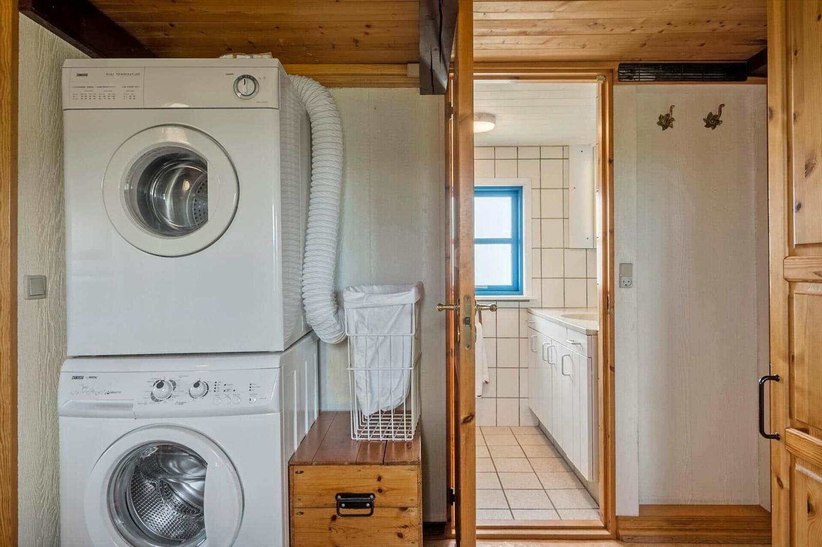 Waschmaschine und Trockner stehen im Flur. Durch Tür ist Bad mit Fenster sichtbar.