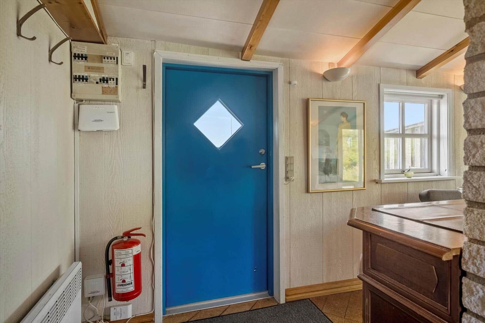 Eingangsbereich mit blauer Tür, Fenster und Holzmöbeln.