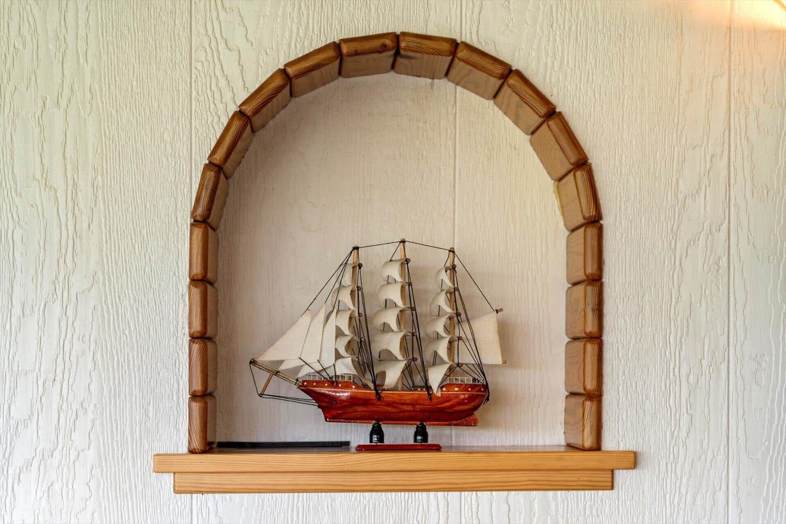 Ein Segelschiffmodell steht auf einem Holzregal unter einem Holzbogen.