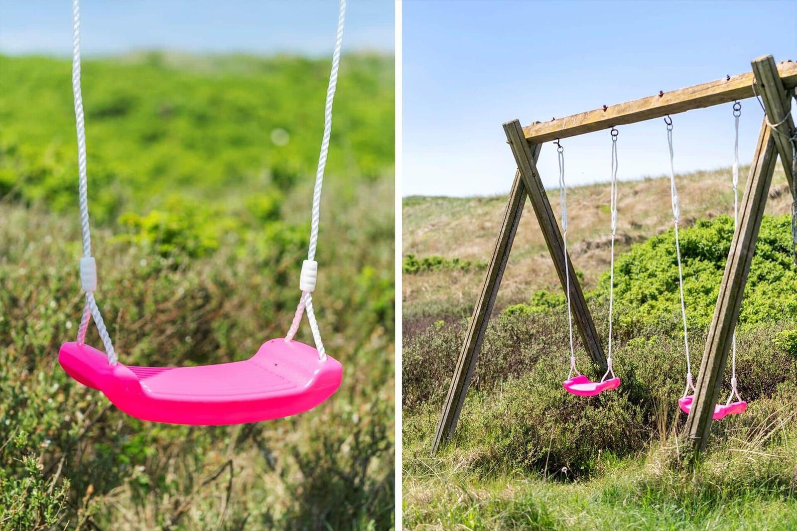 Zwei rosa Schaukeln hängen an einem Holzgestell im Gras.