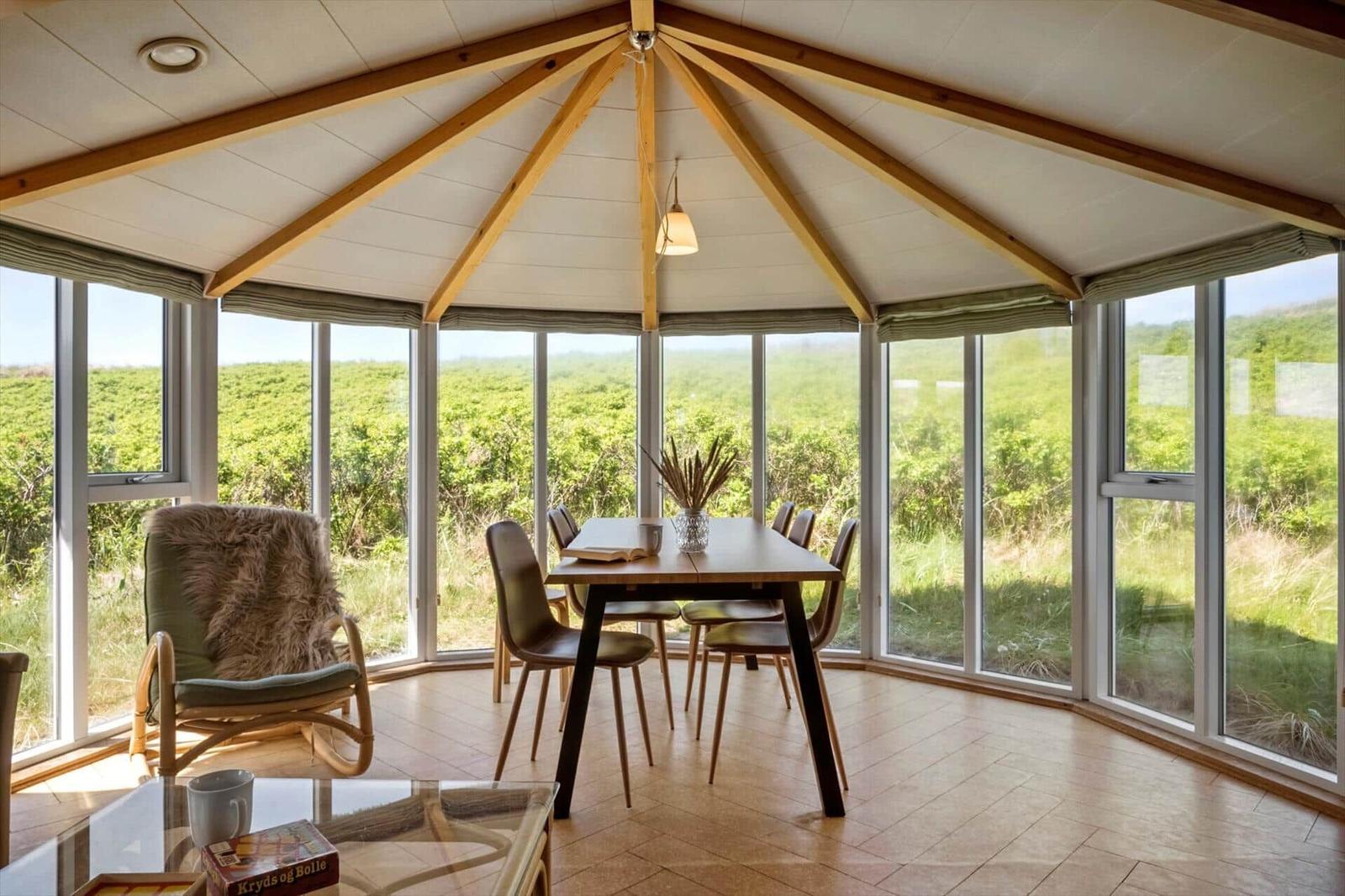 Ein Essbereich mit Tisch, Stühlen und Sessel. Große Fenster bieten Blick auf Grünland.