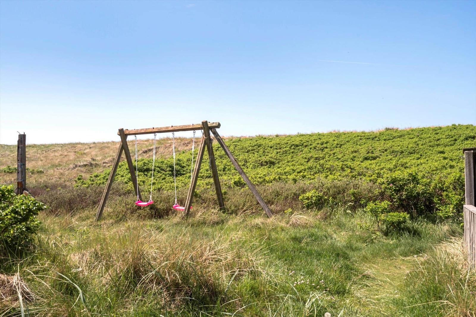 Holzschaukel mit zwei pinken Sitzern in Grasland unter blauem Himmel