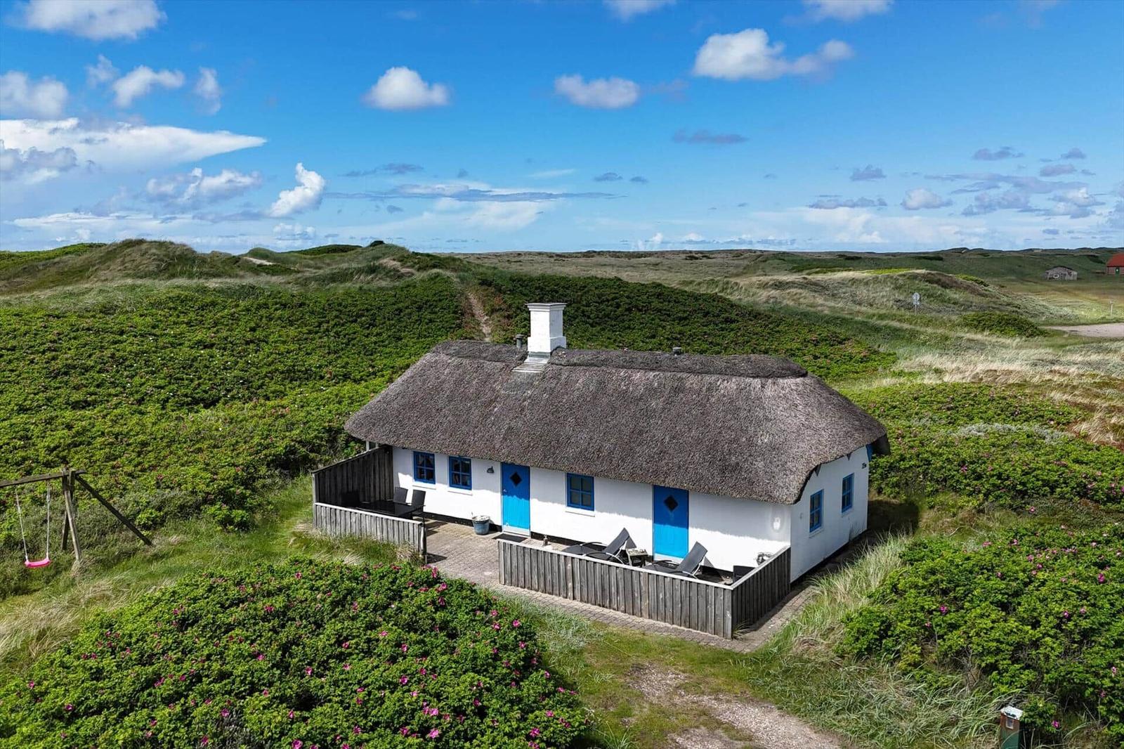 Wohnhaus mit Strohdach und blauen Türen in grüner Landschaft.