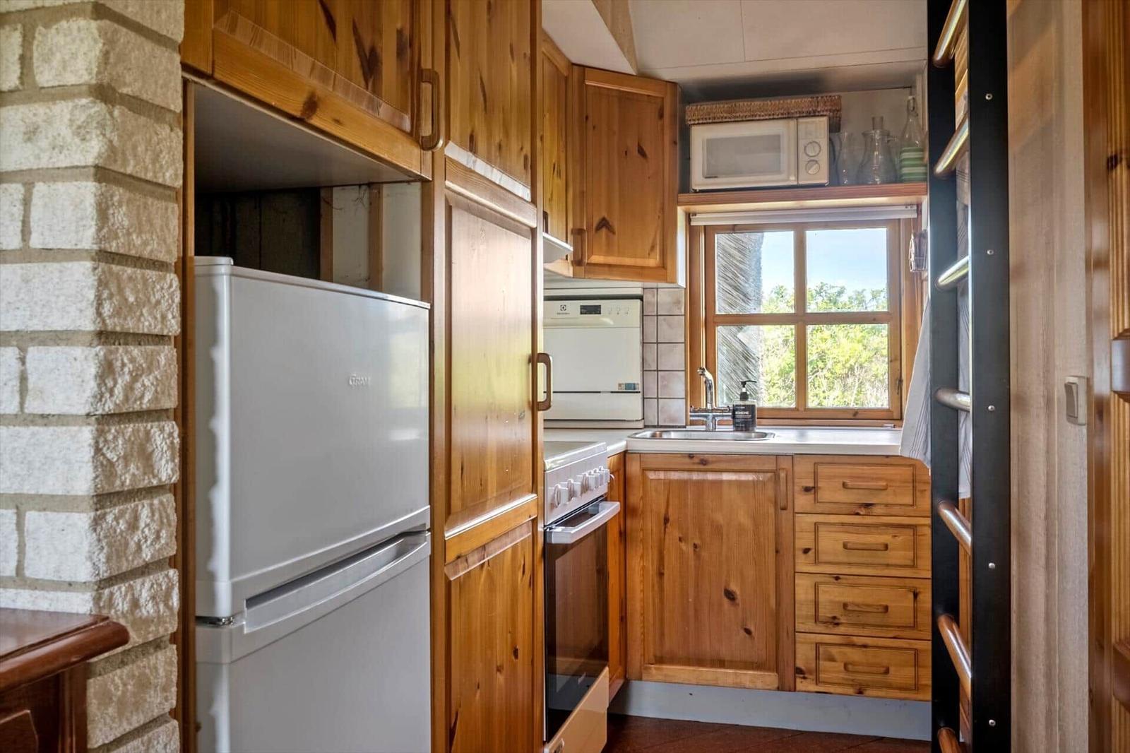 Küche mit Holzschränken, Kühlschrank, Herd und Fenster mit Blick.