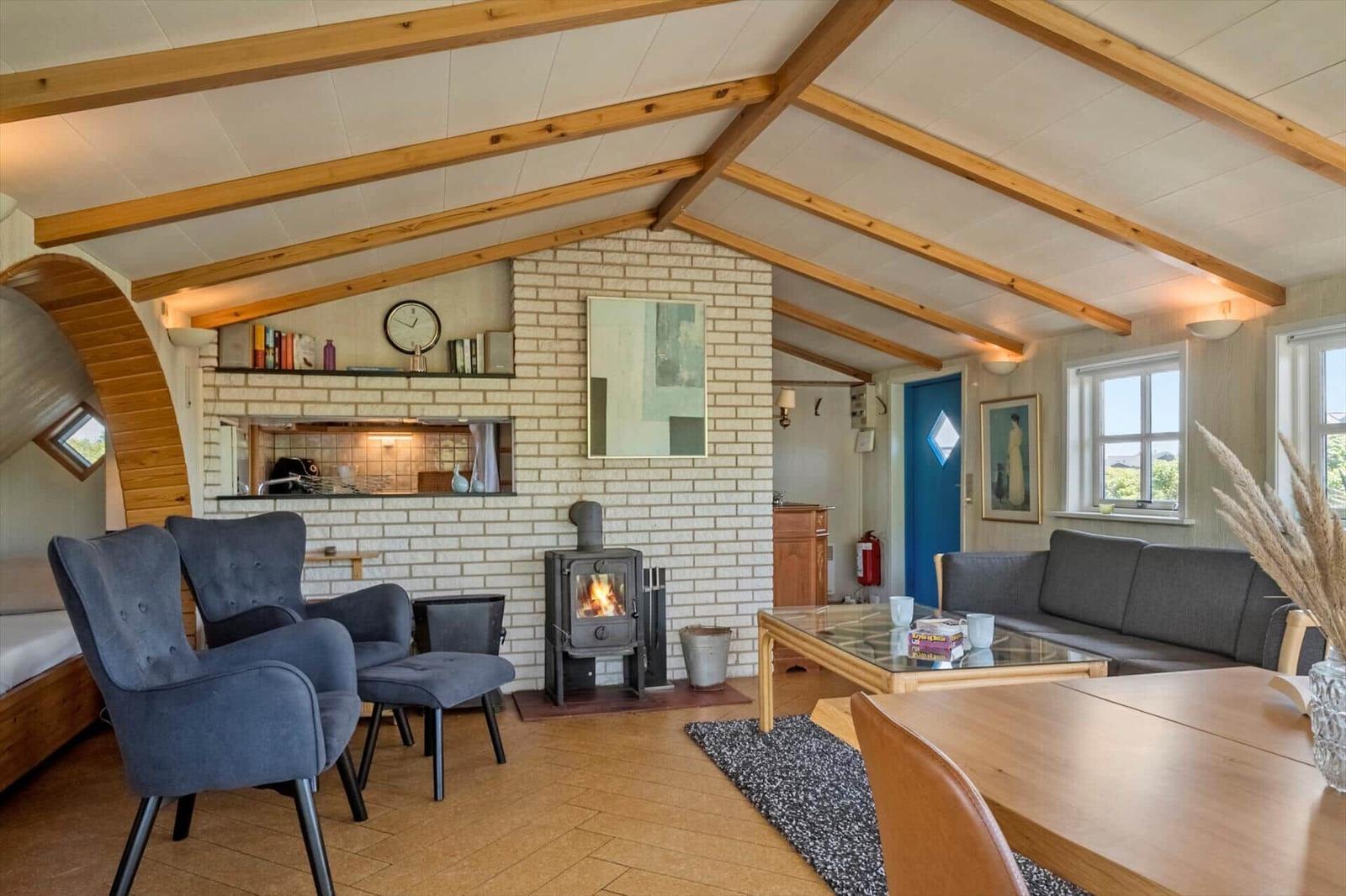 Wohnraum mit Kamin, Sofa und Stühlen unter Holzbalkendecke.