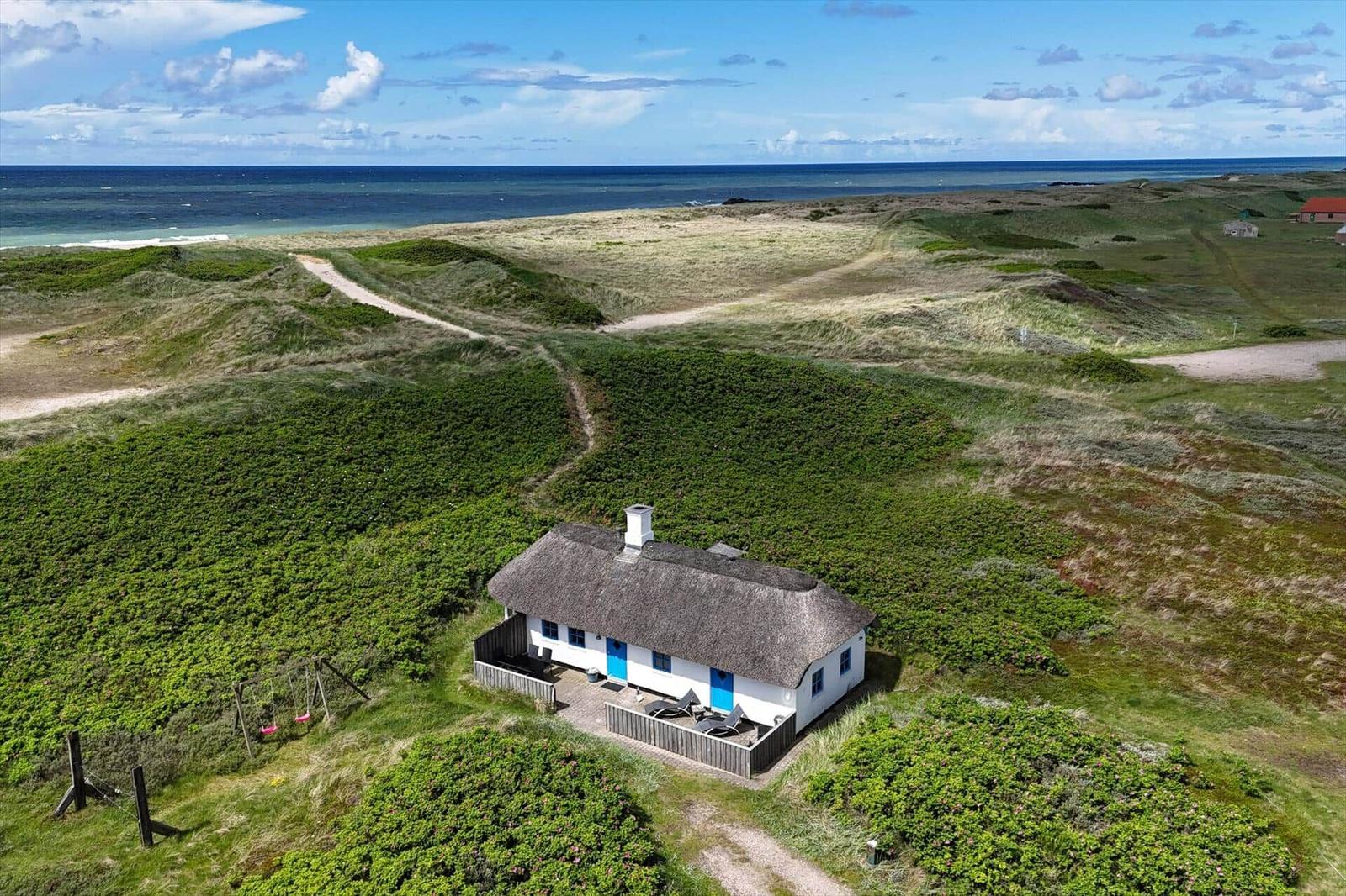 Wohnhaus mit Strohdach und blauen Türen auf grüner Dünenlandschaft mit Blick auf das Meer.