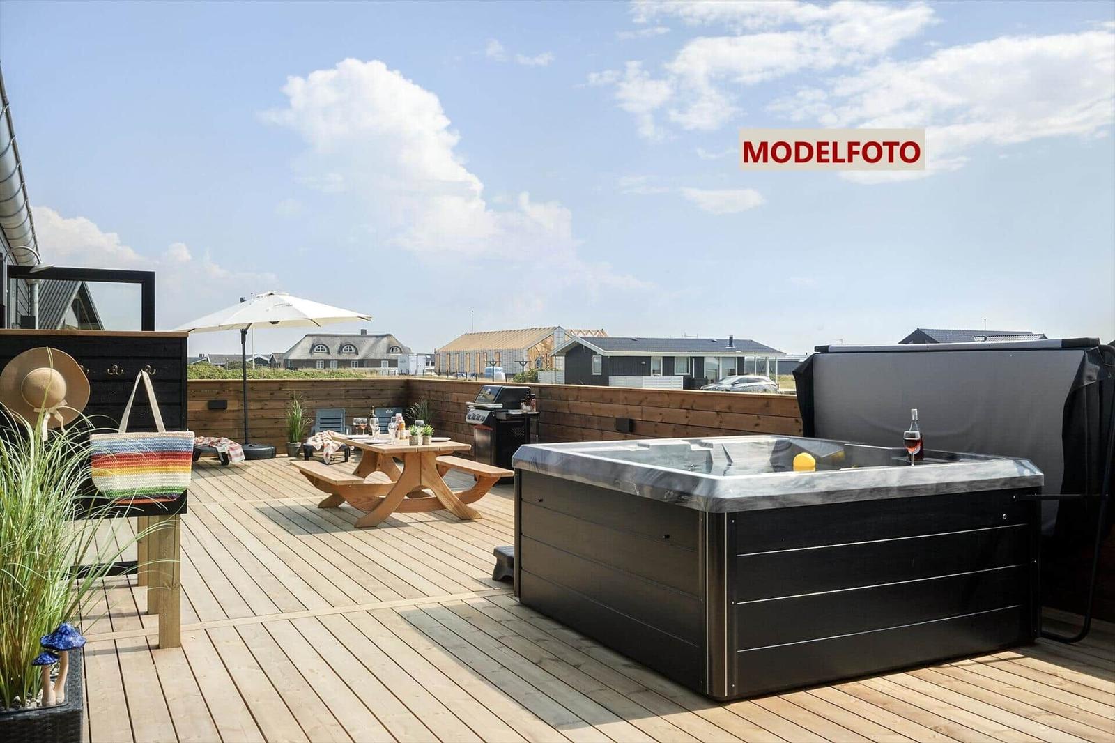 Terrasse mit Whirlpool, Grill und Holztisch unter einem Sonnenschirm.