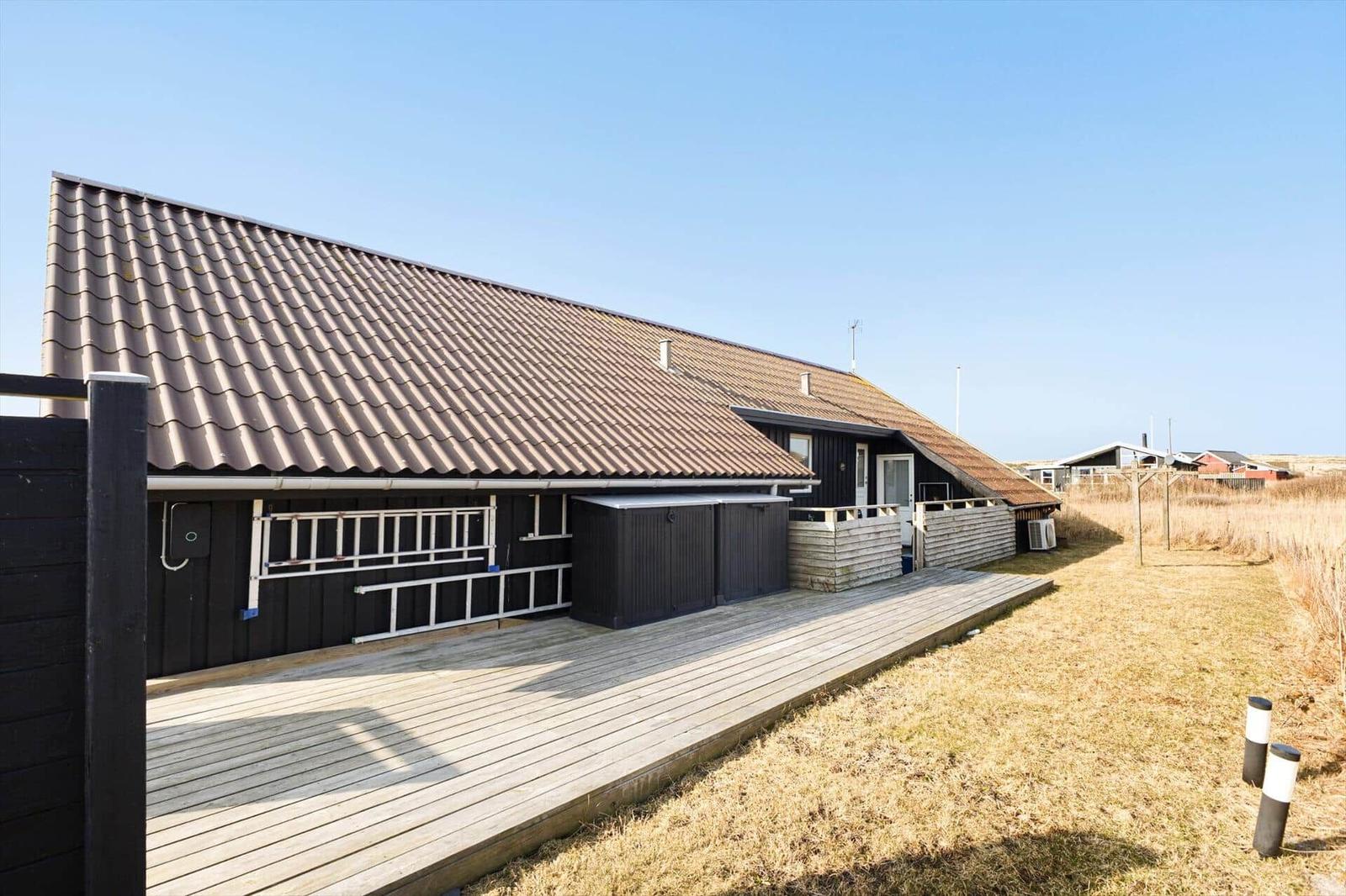 Ein Haus mit Holzterrasse und dunkler Fassade unter blauem Himmel.