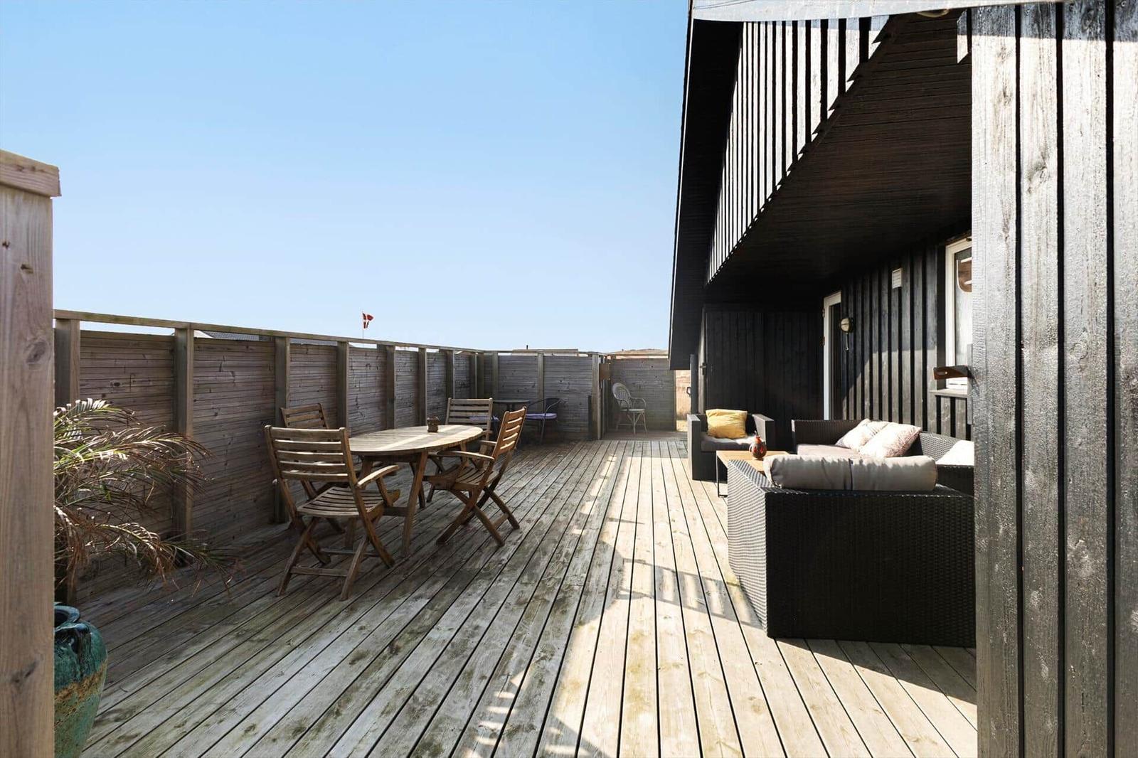 Terrasse mit Holzdecke, Sitzgruppe und Tisch. Hintergrund: Holzwand und Himmel.