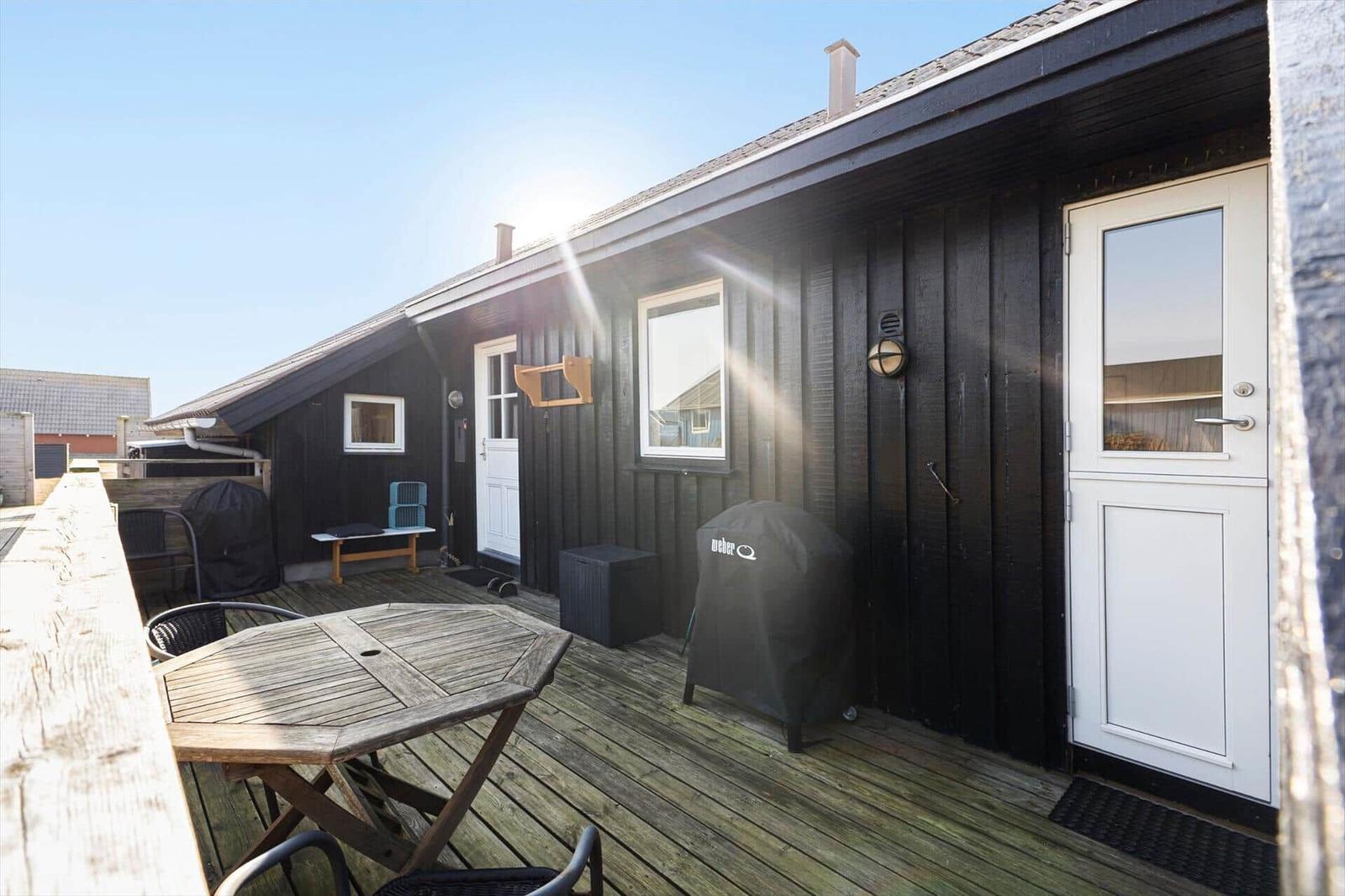 Terrasse mit Tisch und Stühlen vor einem dunklen Holzhaus mit weißen Türen und Fenstern.