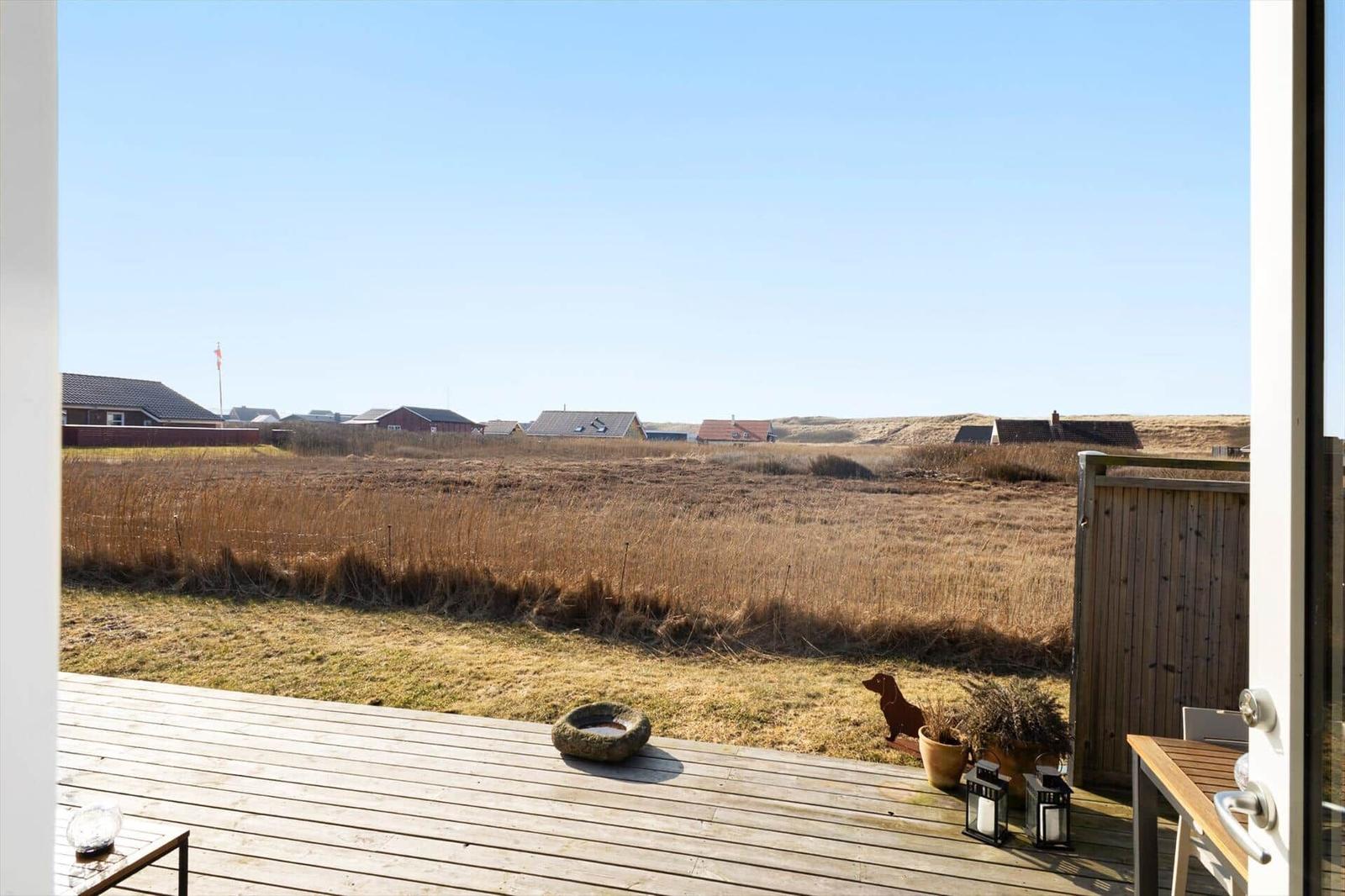 Terrasse mit Holzdielen und Blick auf trockenes Gras und Ferienhäuser