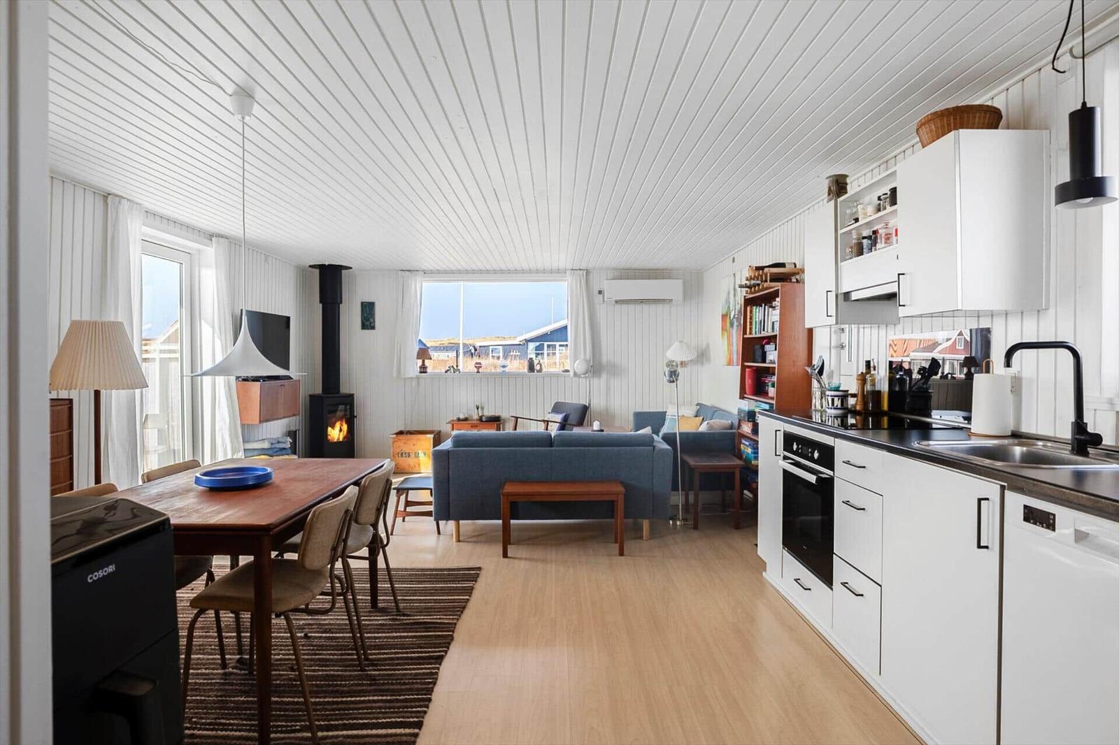 Wohnküche mit Essbereich, Sofa und Kamin. Weiße Wände, Holzboden und Fenster mit Blick.