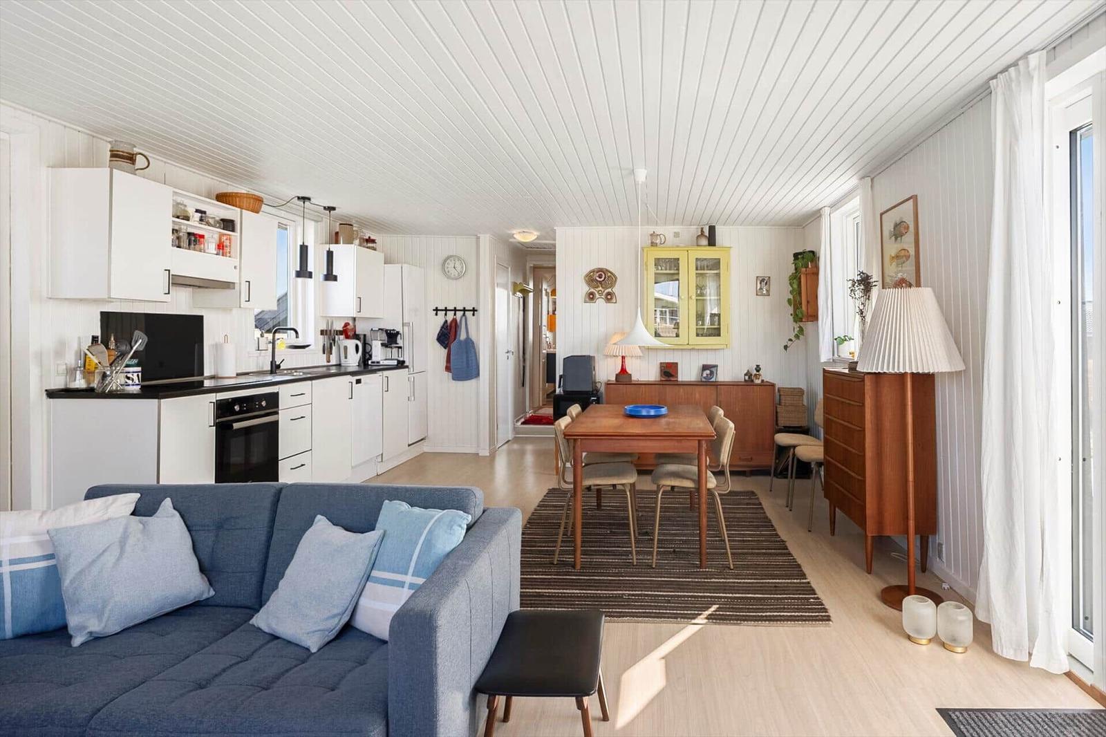Wohn- und Essbereich mit Küche, Sofa und Holztisch. Weiße Wände und Decke.