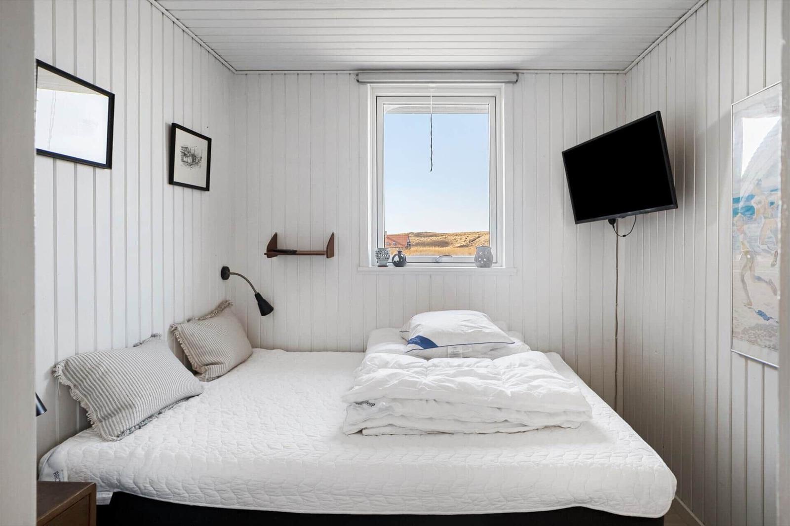 Schlafzimmer mit weißem Bett, Fenster und Wand-TV.
