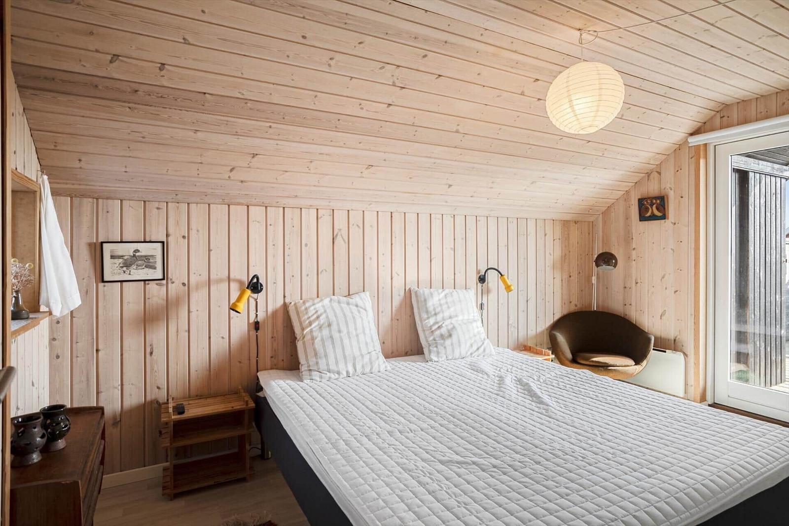 Schlafzimmer mit Holzwand, Bett, Nachttisch und Sessel.