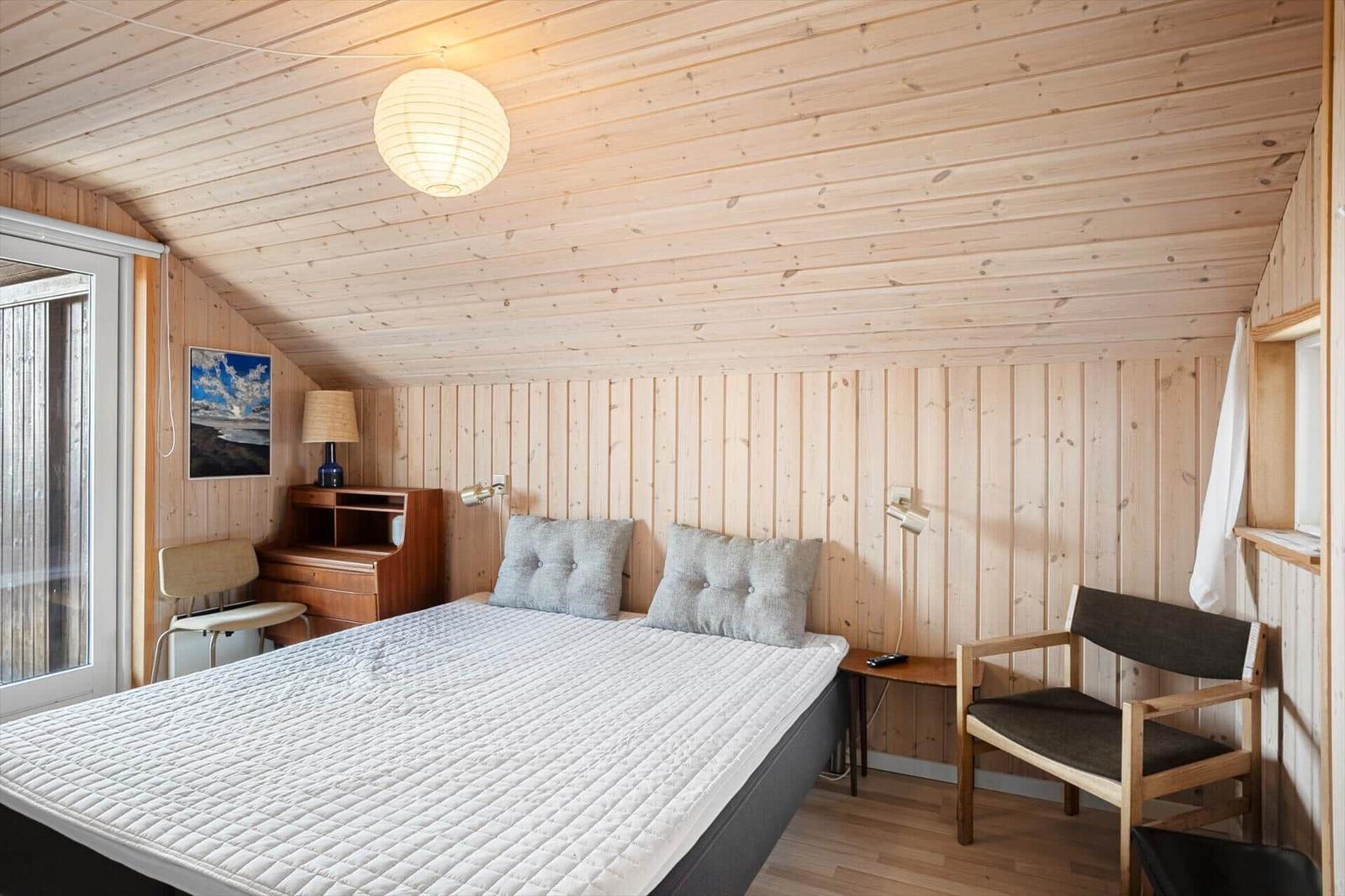 Schlafzimmer mit Holzwand, Bett, Stuhl und Schreibtisch.