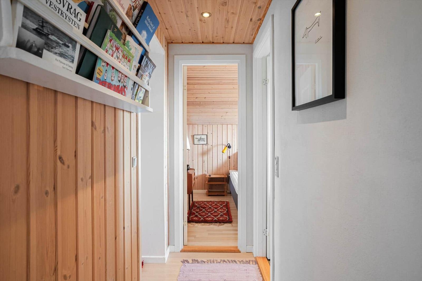 Flur mit Holzwand und Bücherregal, Blick in Schlafzimmer mit Bett und Teppich.