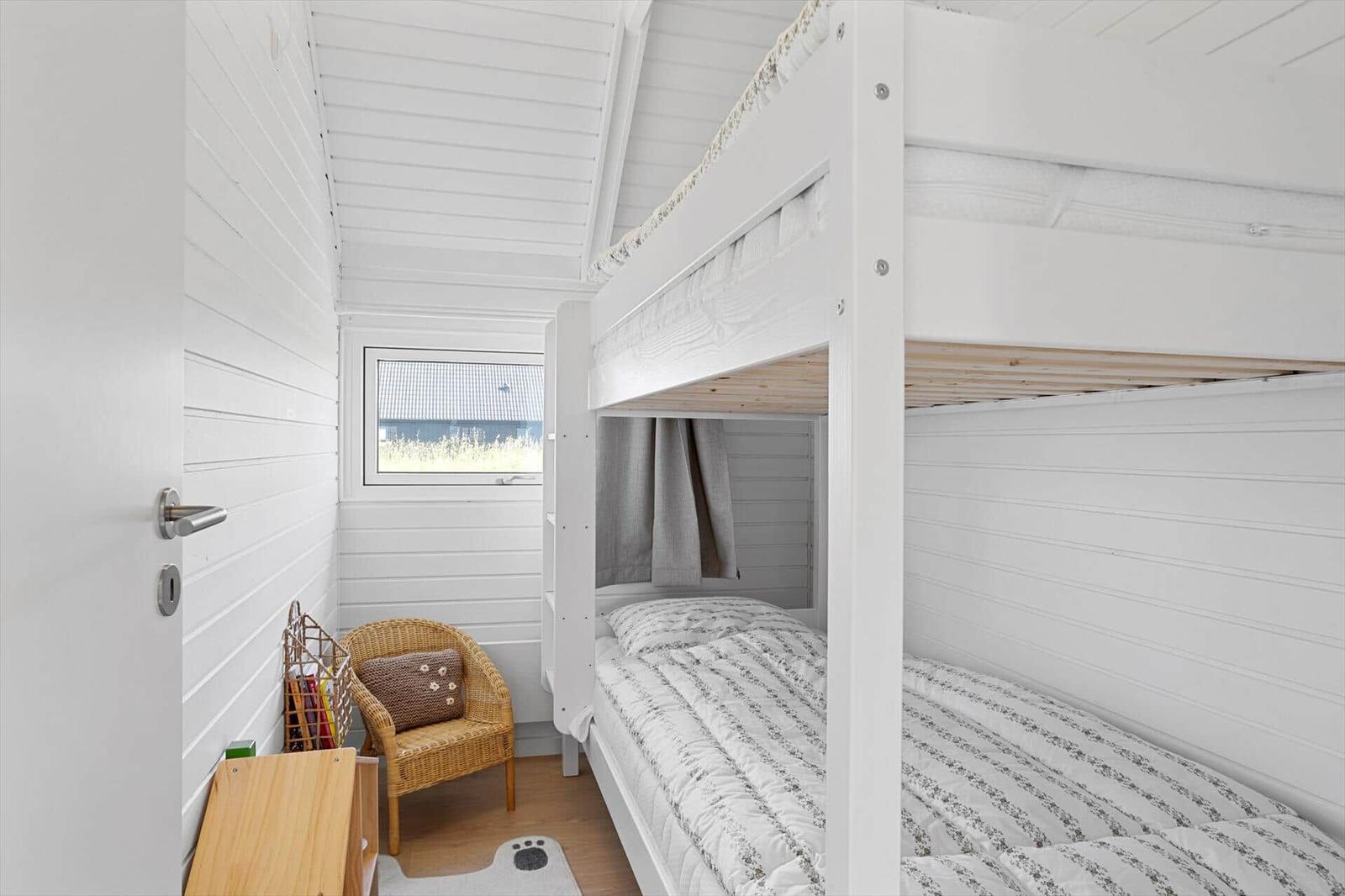 Room with bunk bed, wicker chair, and window with view of grass.