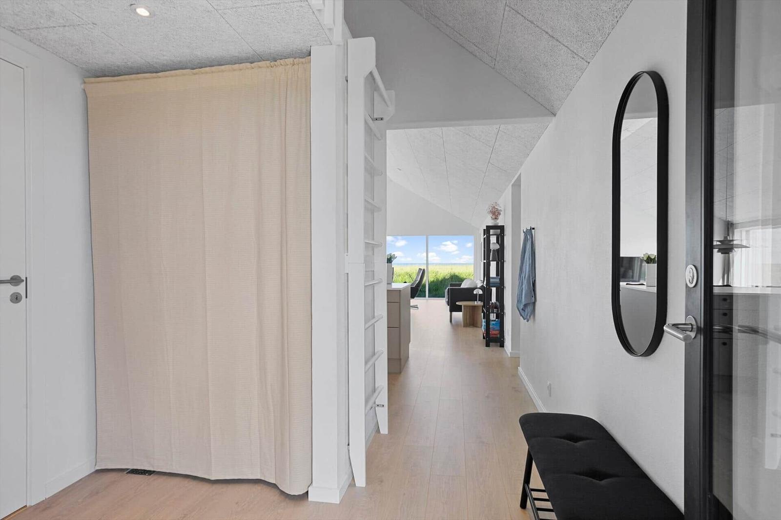 Hallway with curtain, mirror, and bench. Passage to living area with view of green field.
