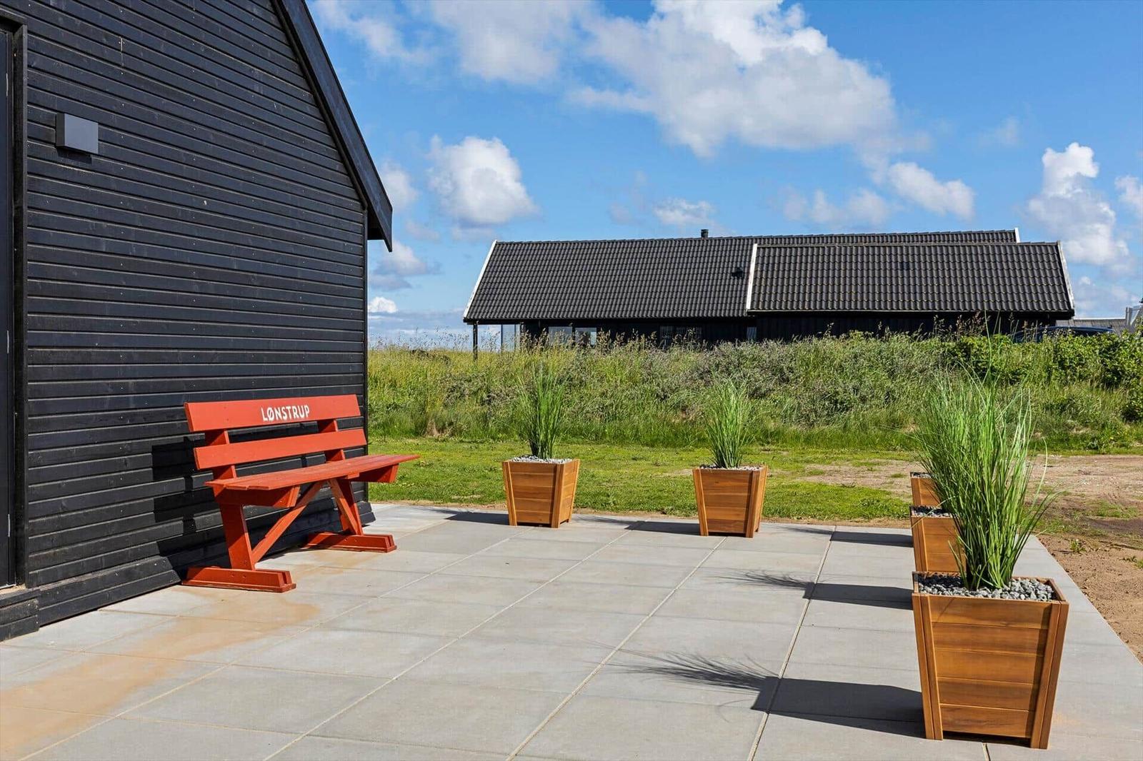 Red bench with inscription beside black house. Stone patio with planter boxes.