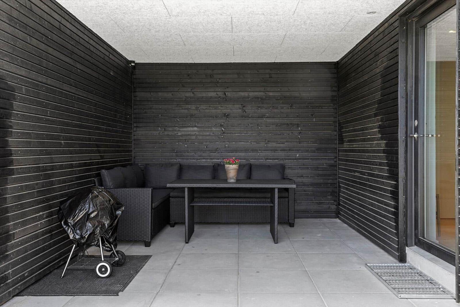 Outdoor area with seating, table, and grill. Black wooden walls and concrete floor.