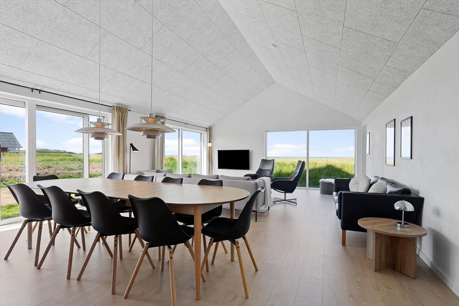 Large room with dining area, sofa, and TV. Large windows offer a view of the landscape.
