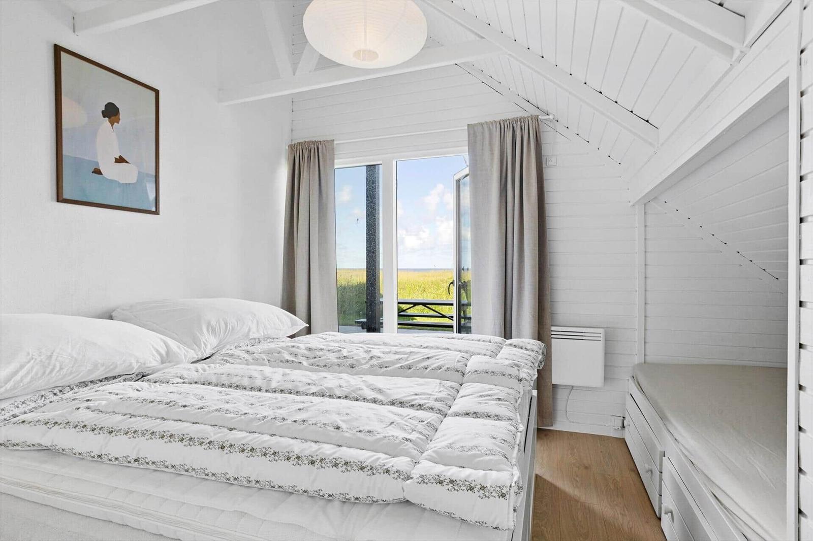 Bedroom with bed, window, and wall art. Wooden floor and white walls.