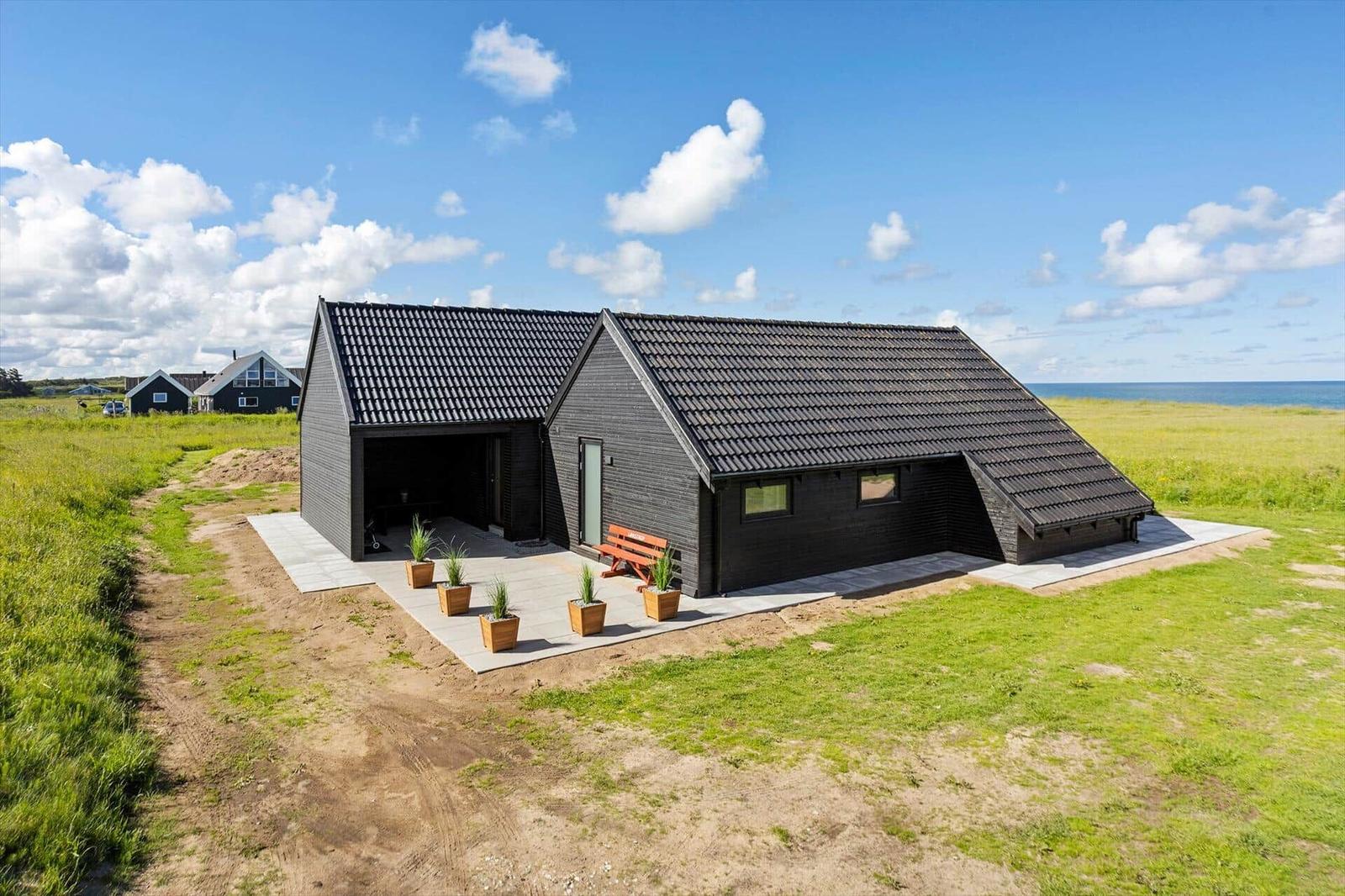 Modern black cabin with terrace, garden, and sea view.