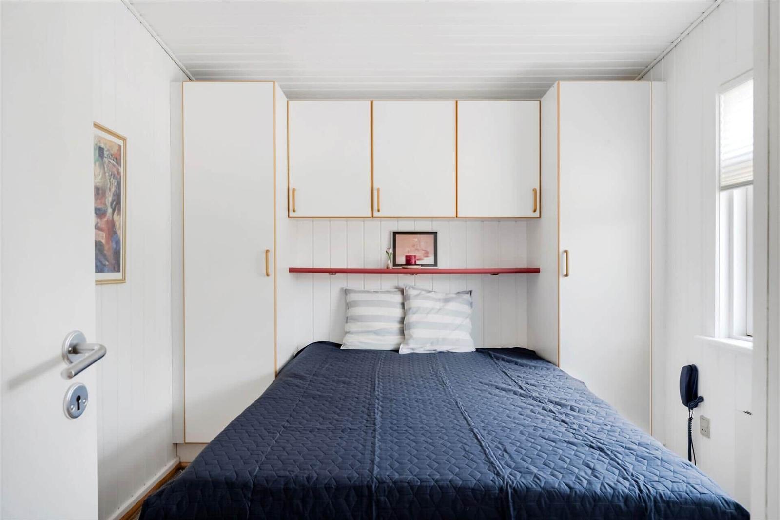 Schlafzimmer mit Bett, weißen Schränken und rotem Regal.